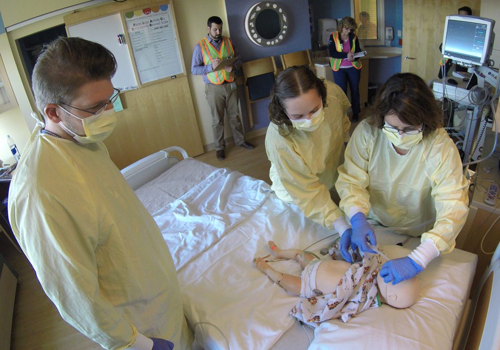 A team of nurses, respiratory therapists and residents respond to a simulated patient while the simulation team observes in the background.